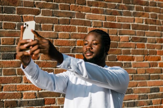 Happy young African American man in dashiki ethnic clothes taking selfie on brick wall background. Millennial generation student and youth