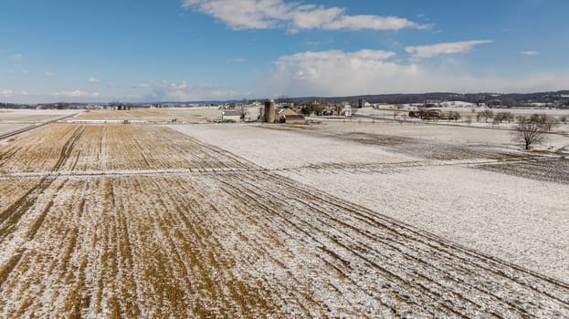 An Aerial View Of Snow-Speckled Agricultural Fields And Farm Buildings.