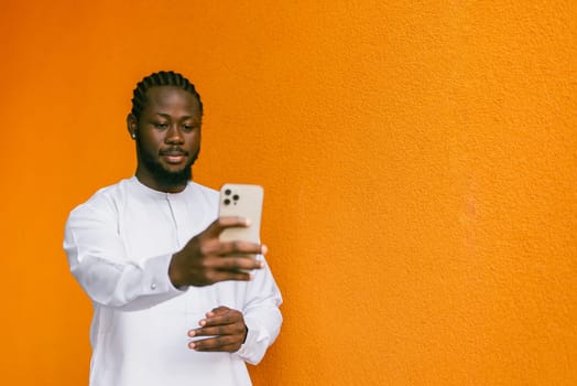 Banner Happy young African American man in dashiki ethnic clothes taking selfie on orange wall background copy space. Millennial generation student and youth