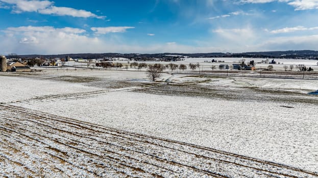 An Aerial View Of Snow-Speckled Agricultural Fields And Farm Buildings.