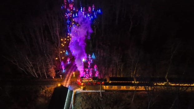 An Aerial View Of A Vibrantly Lit Train Emitting Purple Smoke As It Passes Through A Forested Area At Night.