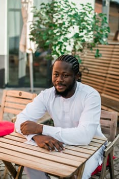 Close up portrait of a happy african american man smiling wearing ethnic dashiki clothes outdoor in summer cafe terrace background. Millennial generation student and youth