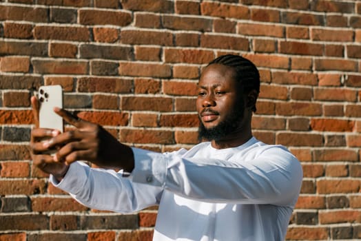 Happy young African American man in dashiki ethnic clothes taking selfie on brick wall background. Millennial generation student and youth