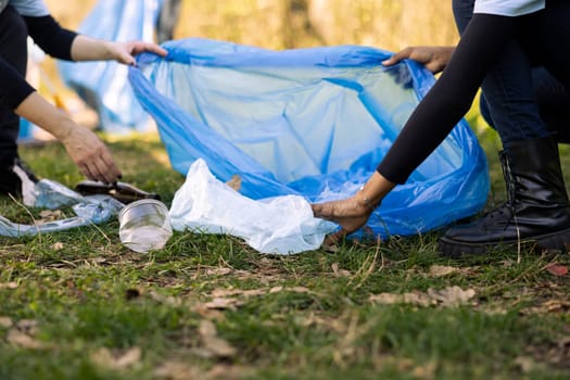 Women volunteers cleaning the forest by picking up trash in bags, recycling plastic waste for a sustainable lifestyle. People collecting garbage, volunteering against pollution.