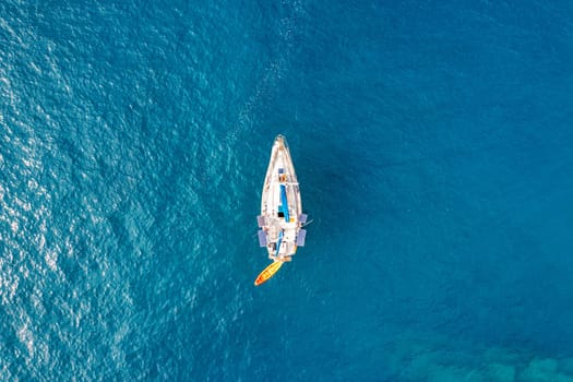 Yacht anchoring in crystal clear turquoise water in front of the tropical island, alternative lifestyle, living on a boat. Aerial view of yacht at anchor on turquoise water, showing luxury, wealth.
