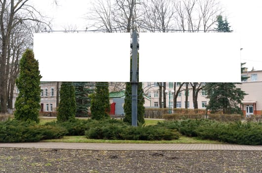 A sizable white sign is positioned on the side of a road, potentially displaying important information for passing drivers.