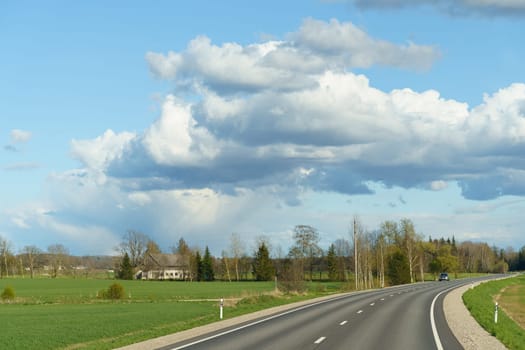 A long road stretches into the distance beneath a sky filled with billowing clouds.