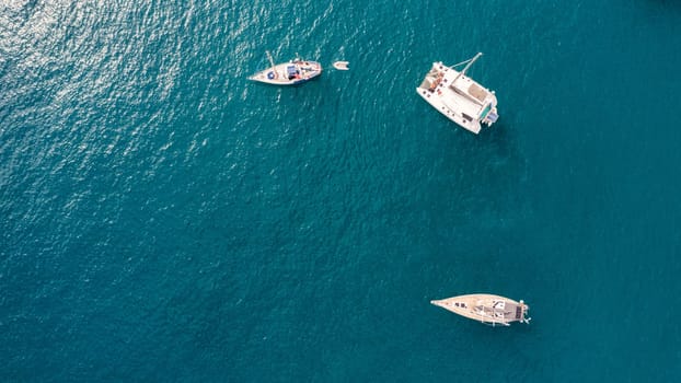 Yacht anchoring in crystal clear turquoise water in front of the tropical island, alternative lifestyle, living on a boat. Aerial view of yacht at anchor on turquoise water, showing luxury, wealth.