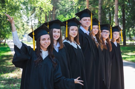 Row of happy young people in graduation gowns outdoors. Students in the park