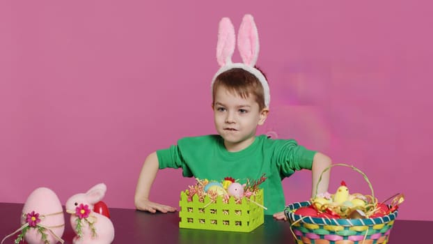 Sweet young boy making colorful arrangements for Easter holiday festivity, putting painted eggs in a handcrafted basket. Ecstatic joyful kid using crafting materials to create decorations. Camera A.