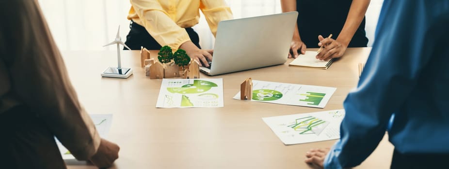 Wooden block represented green city and wind mill represented renewable energy was placed at center of green business meeting table with environmental document. Green business concept. Delineation.