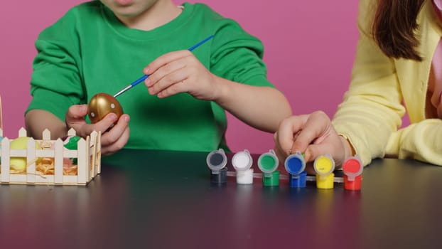 Playful children painting eggs using watercolor and brushes, coloring ornaments for easter sunday celebration. Brother and sister decorating items with stamps and art supplies. Camera A.