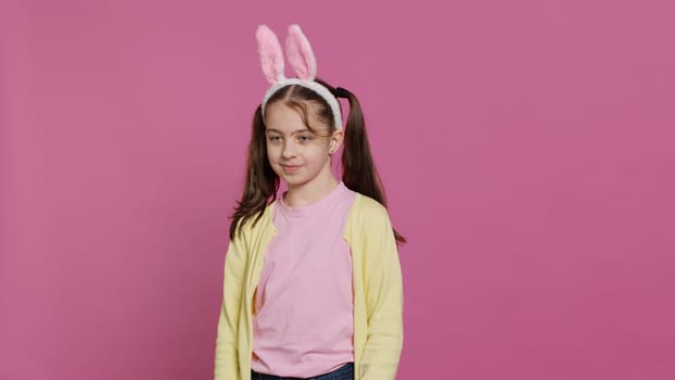 Confident cheery girl showing dance moves in the studio, feeling cheerful and positive about easter holiday festivity. Talented child dancing around and wearing bunny ears. Camera A.