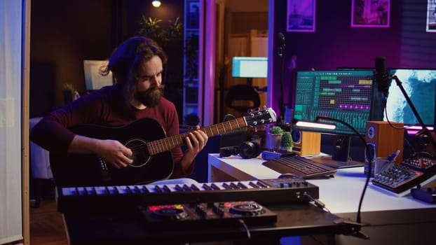 Music producer tuning his acoustic guitar before playing instrument, recording and mixing tunes to create new soundtracks. Singer composing a song using electronic panel controls. Camera B.