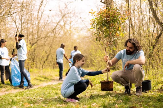 Man and little girl team up and plant a tree together in the woods, preserving the natural environment. People volunteering to help forest ecosystem grow and preserve wildlife.