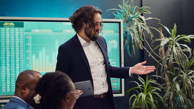 Chief executive officer greeting his employees in a boardroom, starting action review meeting. Manager helps staff members to develop confidence, gain insight and improve themselves. Camera A.