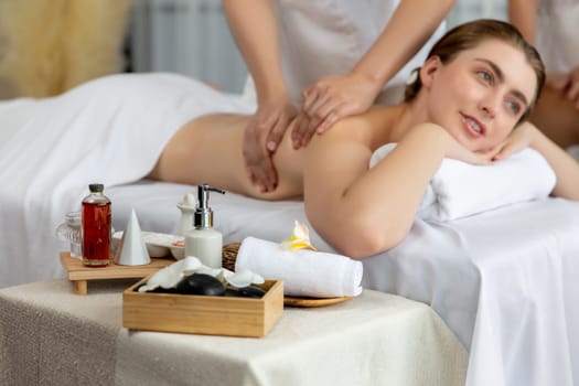 Caucasian couple customer enjoying relaxing anti-stress spa massage and pampering with beauty skin recreation leisure in day light ambient salon spa at luxury resort or hotel. Quiescent