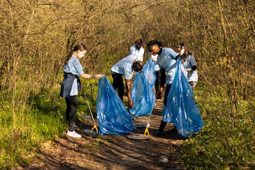 Group of diverse volunteers collecting rubbish and plastic waste, using bags to recycle and gather all junk from the forest habitat. Activists collaborating to clear the woods area from trash.