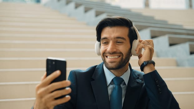 Happy smart business man taking selfie while smiling at smart phone. Closeup image of professional executive manager sitting at stairs while wearing suit and headphone. Creative business. Exultant.