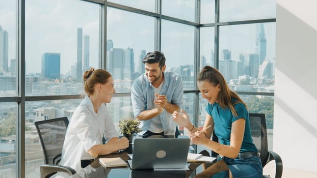 Professional business team receive a good news by using laptop while celebrate their success. Project manager high five and clap hands in front of laptop with colleague at modern office. Tracery