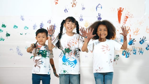 Diverse students put hands up together show colorful stained hands. Group of multicultural learner standing at white background with stained hands while looking at camera in lively mood. Erudition.