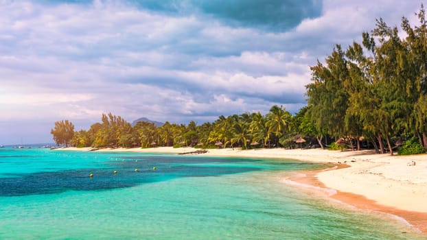 A beach with palm trees and umbrellas on Le morne Brabant beach in Mauriutius. Tropical crystal ocean with Le Morne beach and luxury beach in Mauritius. Le Morne beach with palm trees, white sand and luxury resorts, Mauritius.