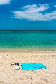 Flip flops and blue beach towel on sand close to the sea