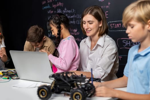 Teacher coding to demonstrate children how to code robots in the STEM class. Children fun to watch how teacher coding with confident only boy in blue shirt taking note with serious look. Erudition.