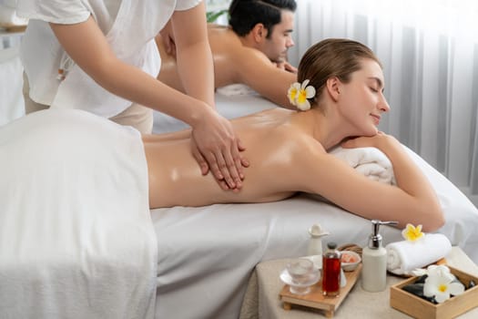 Caucasian couple customer enjoying relaxing anti-stress spa massage and pampering with beauty skin recreation leisure in day light ambient salon spa at luxury resort or hotel. Quiescent