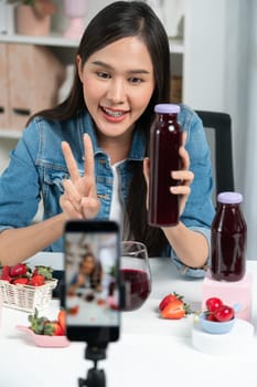 Smiling young beautiful Asian reviewing tasty mixed strawberry and cherry juice detox drinks, showing healthy product to promote for special promotion selling on social media online record. Stratagem.