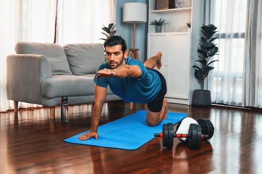 Flexible and dexterity man in sportswear doing yoga position in meditation posture on exercising mat at home. Healthy gaiety home yoga lifestyle with peaceful mind and serenity.