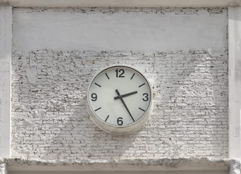 Round white watch face with numbers hanging on white brick wall. Clock dial face in front of brick wall, Space for text, Selective focus.