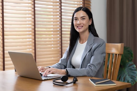 Female call center operator or customer service helpdesk staff working on workspace while talking on the headset to provide assistance for customer. Professional modern business service. Blithe