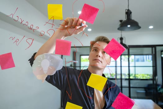 Professional caucasian businessman writing marketing idea by using mind map and sticky notes on glass board at modern meeting room. Creative business and planing concept. Closeup. Immaculate.