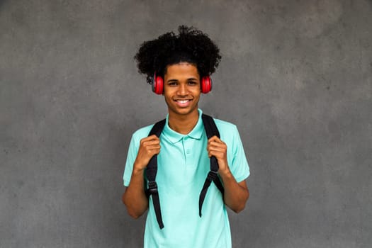Happy teen African American boy with afro hairstyle looking at camera wearing headphones and backpack. Lifestyle concept.