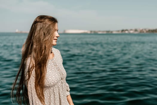 A woman is walking on the beach wearing a dress. The water is calm and the sky is clear