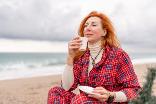 Sea Lady in plaid shirt with a mug in her hands enjoys beach with Christmas tree. Coastal area. Christmas, New Year holidays concep.