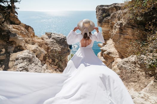 A woman in a white dress is walking on a rocky beach near the ocean. The scene is serene and peaceful, with the woman's dress flowing in the wind