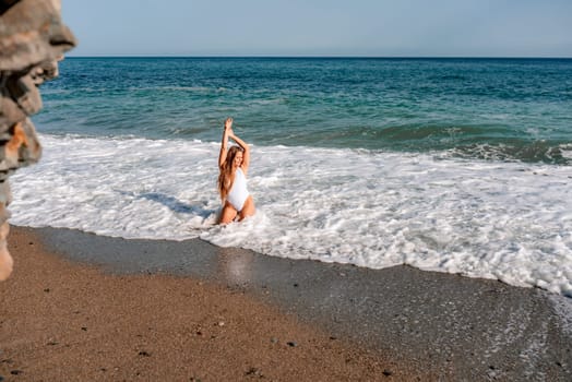 Happy woman in bikini sits on the sea beach. Tanned girl sunbathing on a beautiful shore. Summer vacation or holiday travel concept.