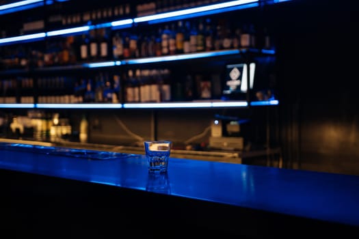 A bar with a blue counter and shelves of liquor. The bar is empty and the lights are on