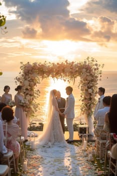 Couple stands hand in hand during their beach wedding ceremony at sunset, with a beautiful ocean backdrop and floral decorations