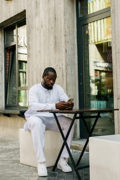 African american man checks cell phone in the street cafe in summer day. Millennial generation and gen z people. Social networks and dating app