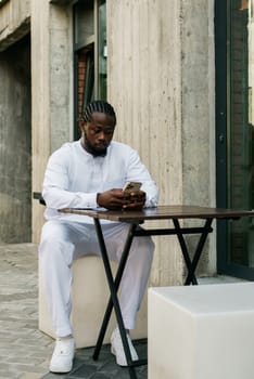 African american man checks cell phone in the street cafe in summer day. Millennial generation and gen z people. Social networks and dating app