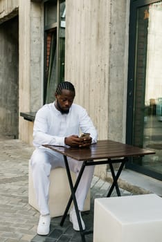 African american man checks cell phone in the street cafe in summer day. Millennial generation and gen z people. Social networks and dating app