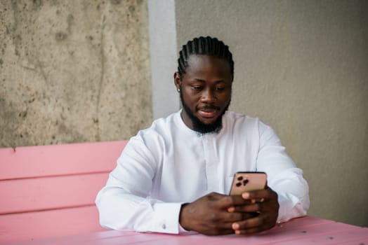 African american man checks cell phone in the street cafe in summer day. Millennial generation and gen z people. Social networks and dating app