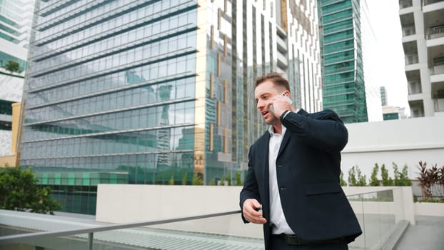 Skilled businessman talking to marketing team about marketing strategy by using phone while standing at skyscraper. Happy manager calling colleague about increasing sales at modern urban city. Urbane.