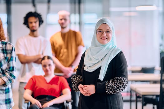 A diverse group of young business people walking a corridor in the glass-enclosed office of a modern startup, including a person in a wheelchair and a woman wearing a hijab.