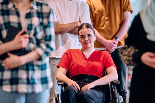 A diverse group of young business people walking a corridor in the glass-enclosed office of a modern startup, including a person in a wheelchair and a woman wearing a hijab.