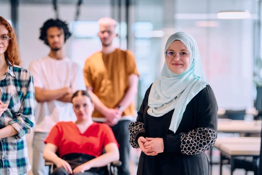 A diverse group of young business people walking a corridor in the glass-enclosed office of a modern startup, including a person in a wheelchair and a woman wearing a hijab.