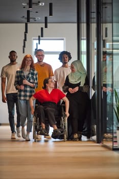 people walking a corridor in the glass-enclosed office of a modern startup, including a person in a wheelchair and a woman wearing a hijab.